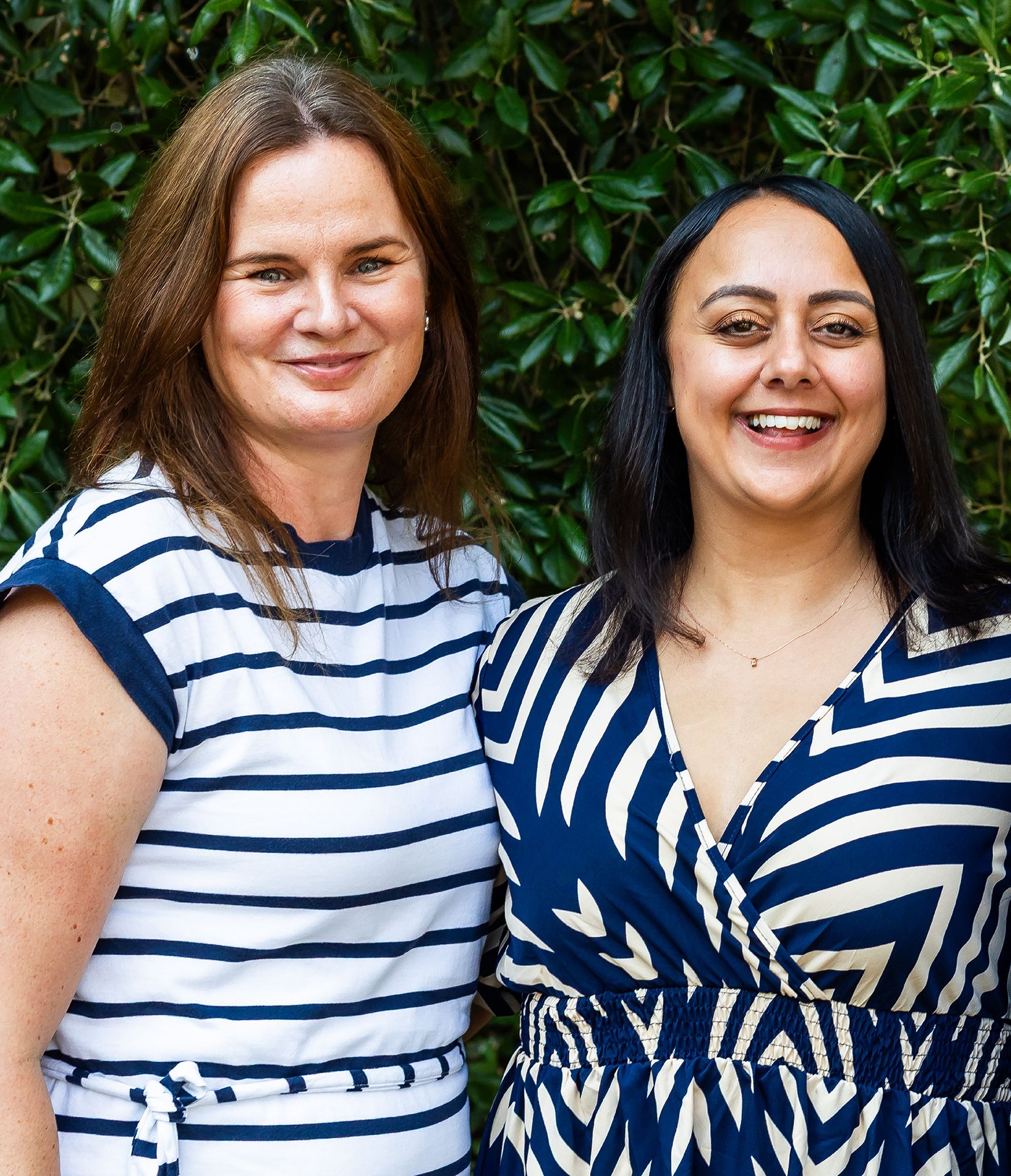 Emma Culver and Bianca Rodriguez Jacobs standing together in front of green bush.